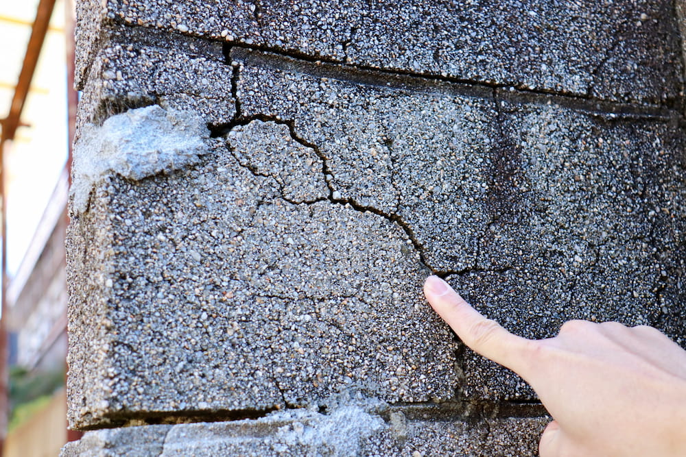 ひび割れたブロック塀を指差して点検する様子