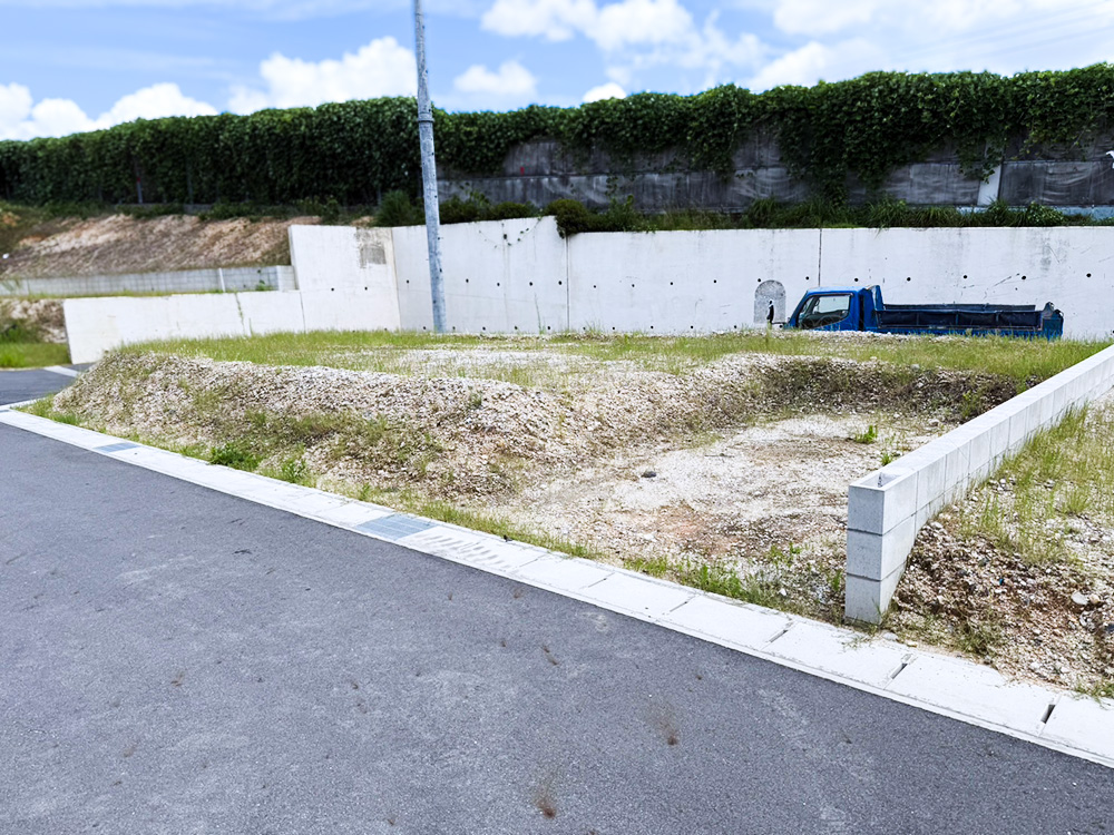 造成工事施工前の土地を擁壁側から撮影。雑草が生い茂り整地が必要な状態で、奥には作業用トラックが見える
