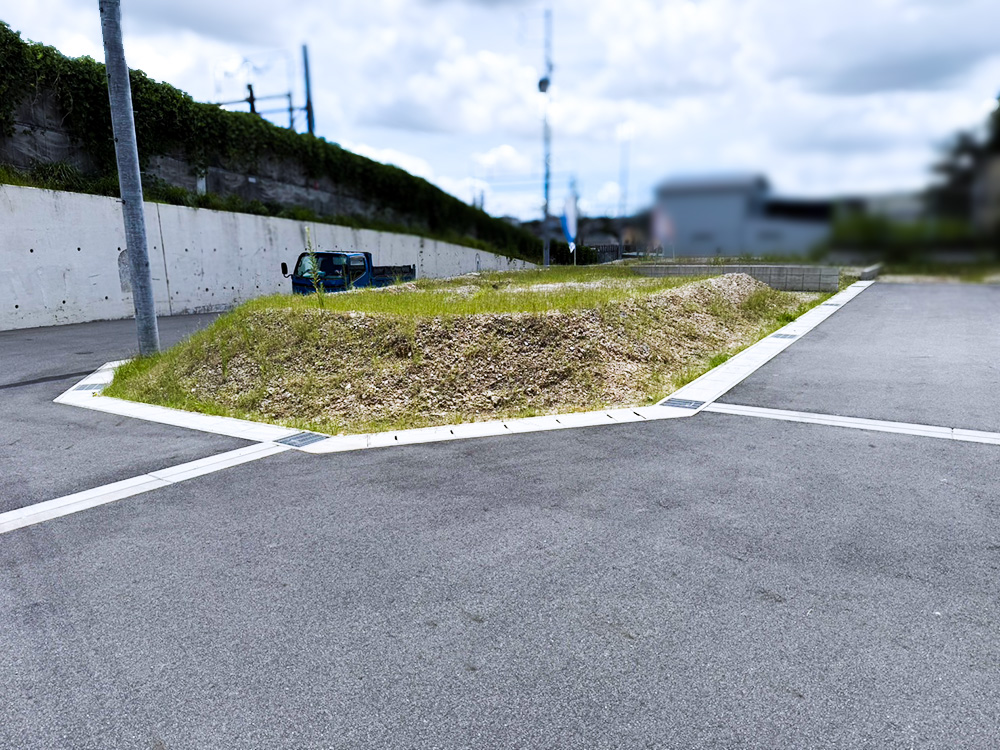 地鎮祭前の造成工事施工前の様子。雑草と砂利が混在する未整地の土地で、周囲は道路とコンクリート擁壁に囲まれている