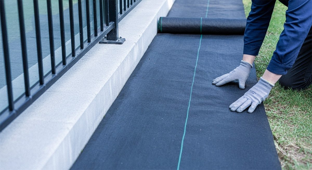 フェンス沿いに防草シートを敷設している作業の様子