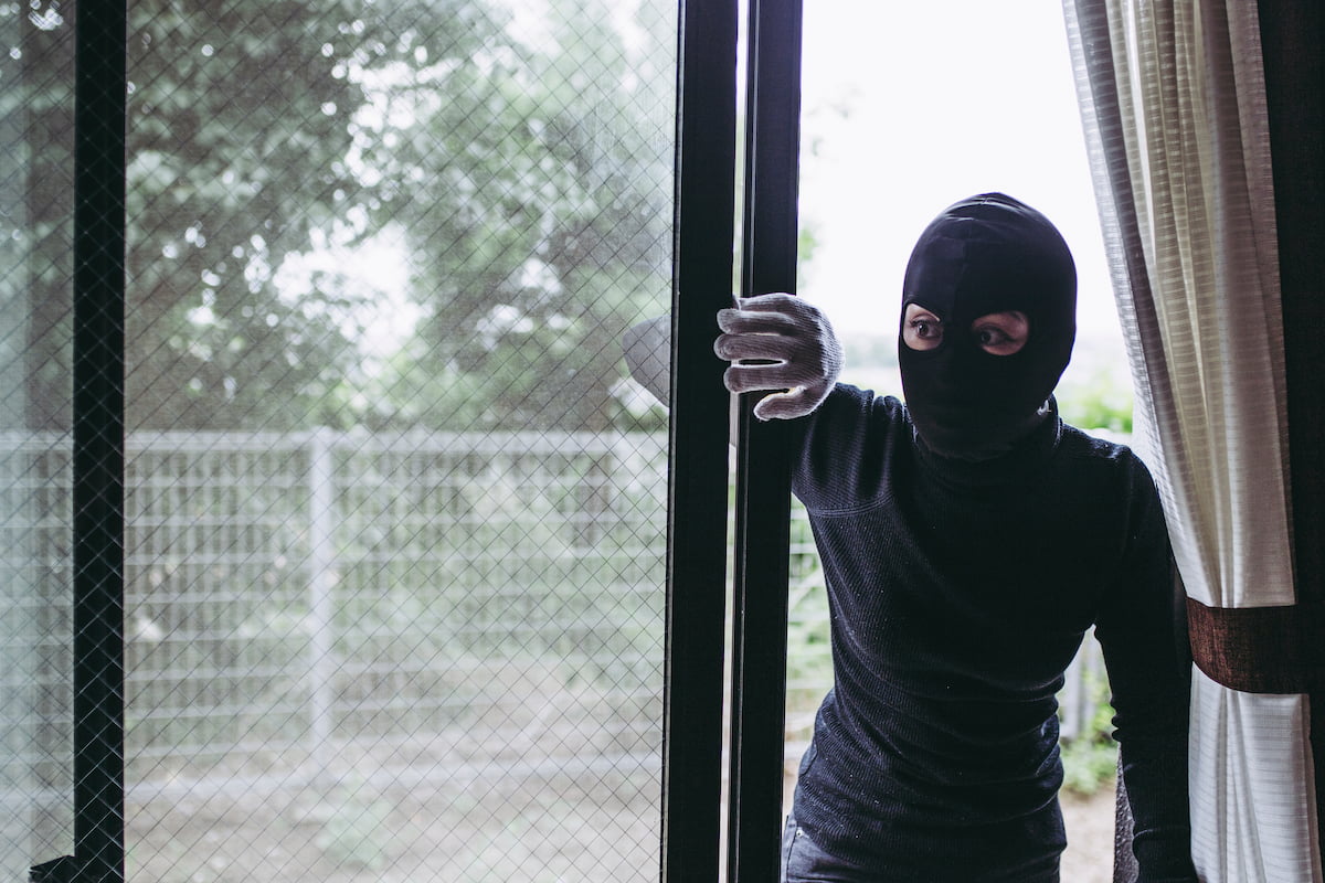 窓から侵入しようとする不審者、空き家への侵入窃盗の危険性を示す防犯対策の重要性