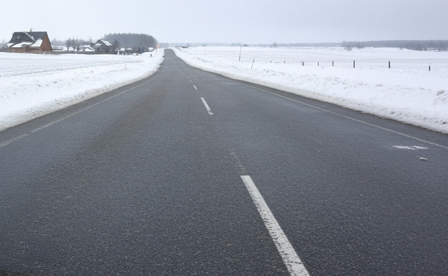 雪景色の中で一見乾いているように見える危険なブラックアイス現象の道路、凍結した路面が黒く見える冬の駐車場の危険性を示す