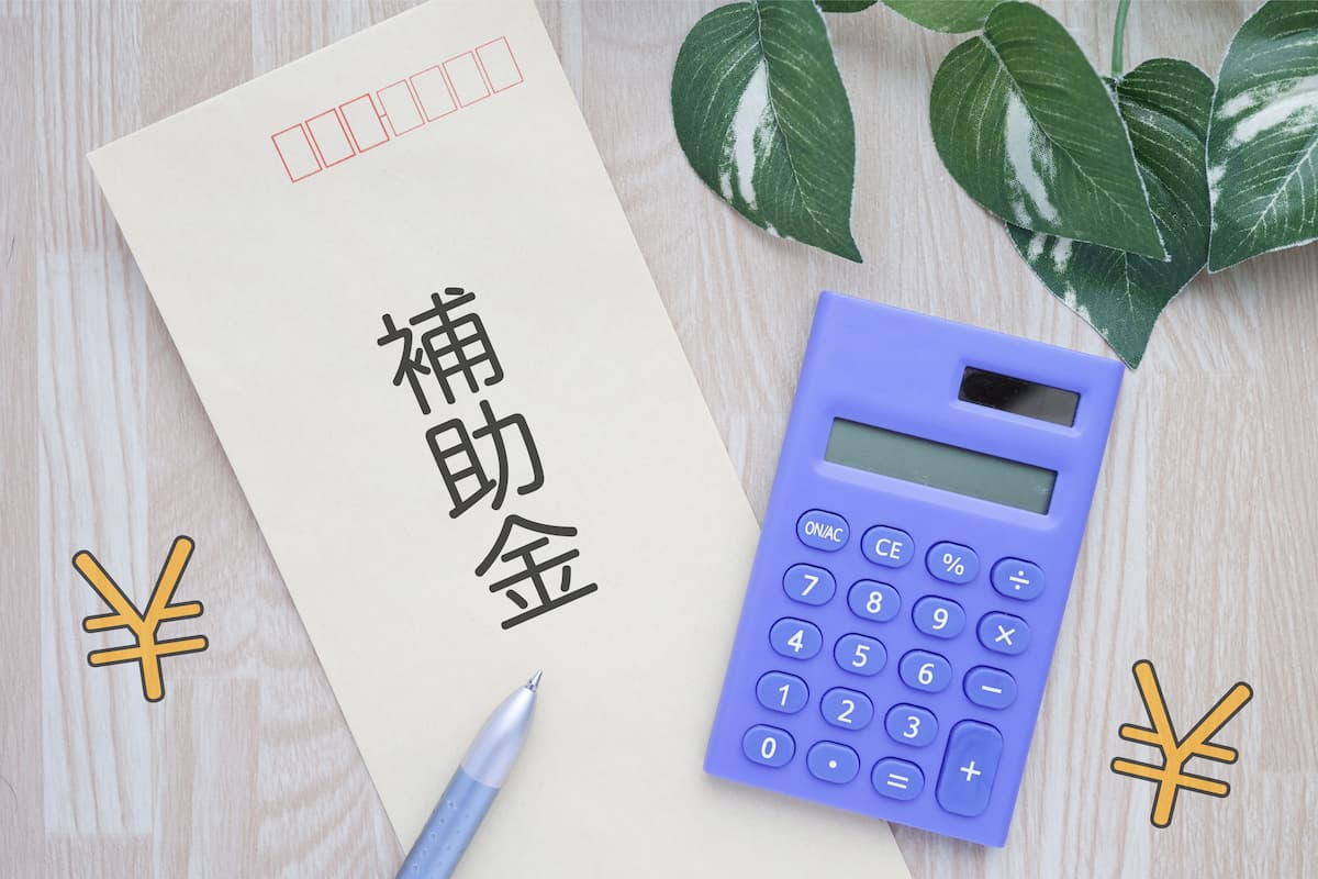 補助金と書かれた封筒と青い電卓、リフォーム補助金の計算と申請準備を表す書類とペン