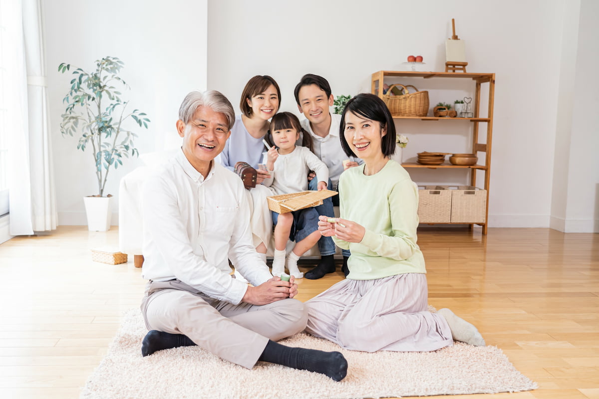 年末年始に実家に集まった三世代家族。リビングで笑顔で過ごす祖父母と子ども夫婦、孫の様子