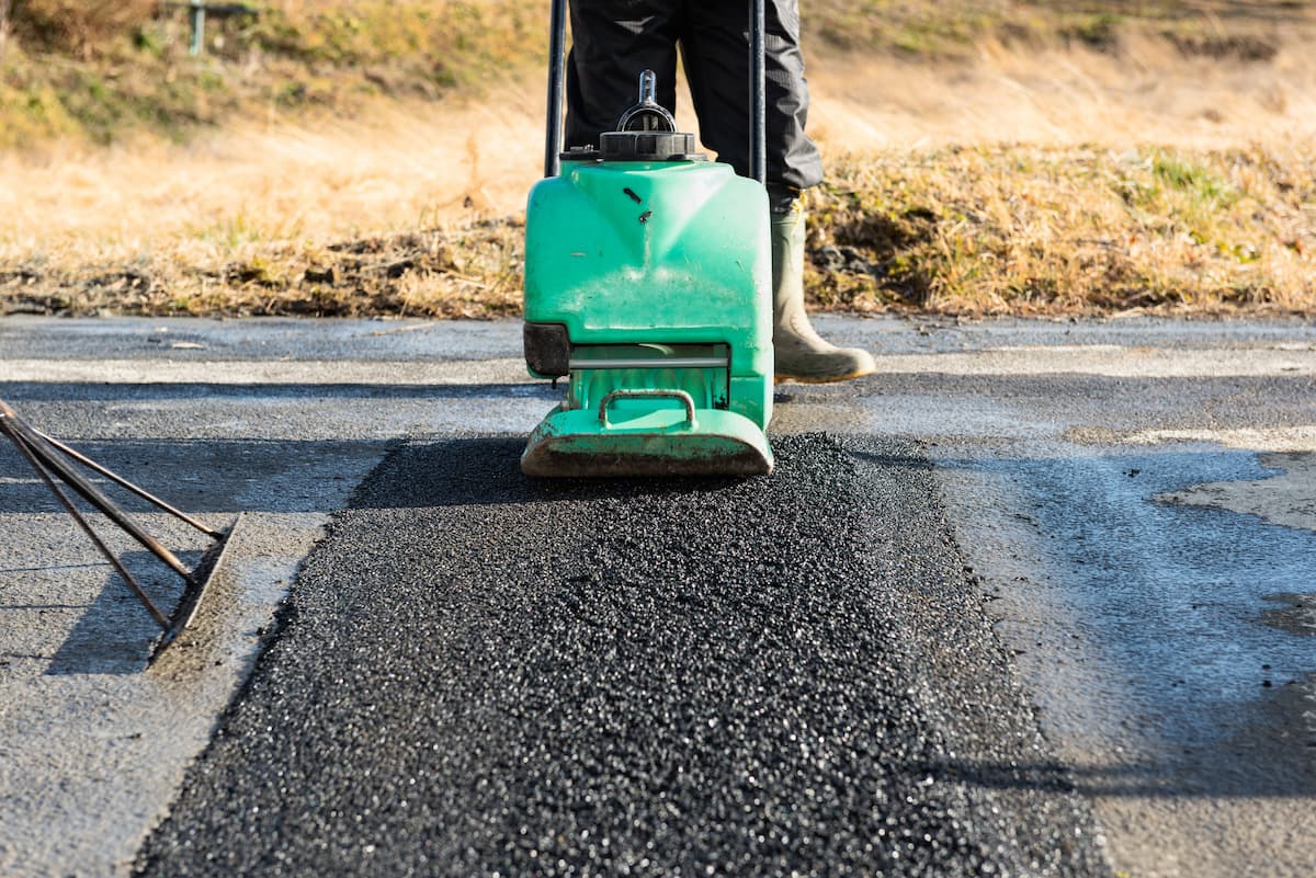 アスファルト舗装の転圧作業。プレートコンパクターで新しいアスファルトを締め固めている様子。