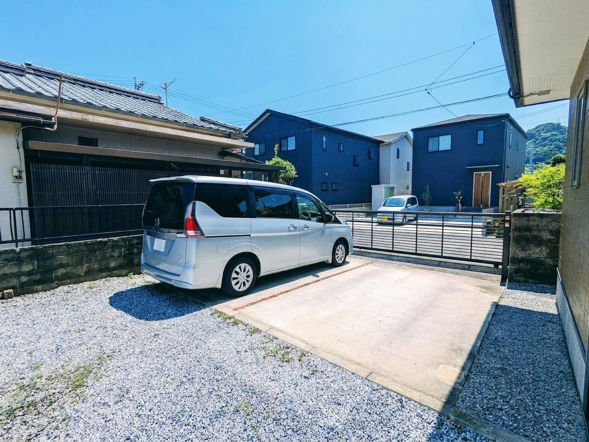 夏の強い日差しを浴びて照り返しが強くなっているコンクリートと砂利の駐車場